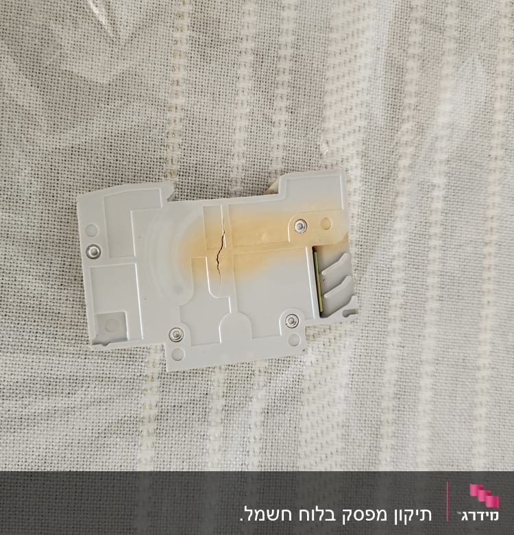 רכיב חשמלי לבן עם סדק על רקע בד אפור